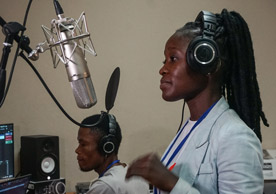 Liberian woman preparing to sing into studio microphone with man recording in the background